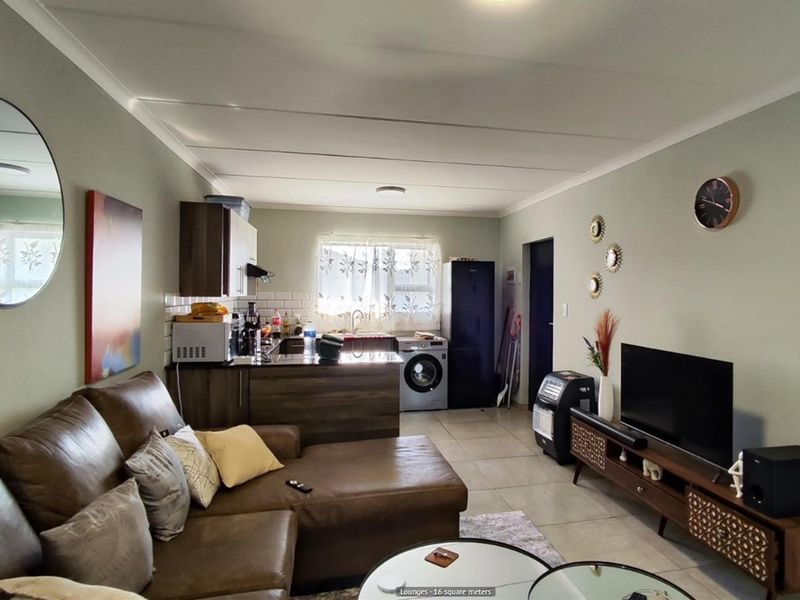 An open-plan living area featuring a compact kitchen with built-in cabinetry, tiled flooring, and a functional layout suitable for modern apartment living.