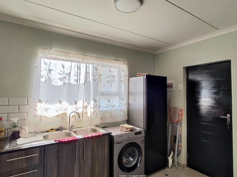 Functional kitchen area featuring a double basin sink, tiled backsplash, and dedicated space for laundry appliances.