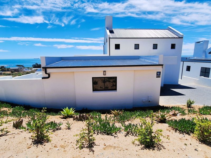Rear view of a modern white house with a corrugated metal roof, paved driveway, and coastal views.