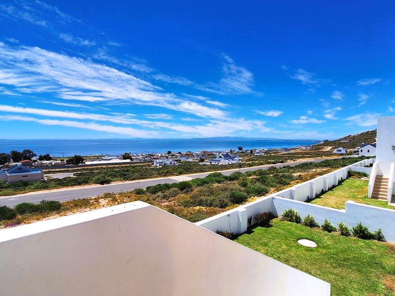 Elevated coastal view overlooking the surrounding neighborhood, landscaped garden areas, and the ocean horizon from a modern balcony.