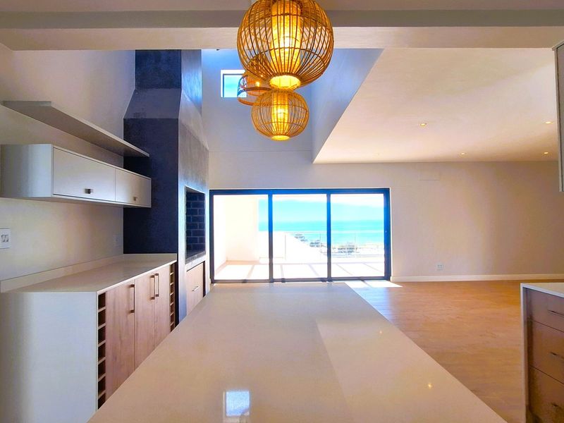 Spacious open-plan living and kitchen area featuring modern cabinetry, stone countertops, a built-in fireplace, and large sliding doors opening to a scenic view.