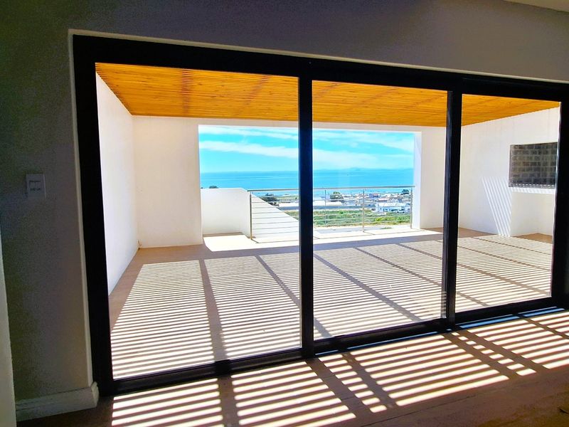 Spacious covered balcony featuring a timber slat ceiling, built-in braai, and stainless steel balustrade, offering expansive ocean views through large sliding glass doors.