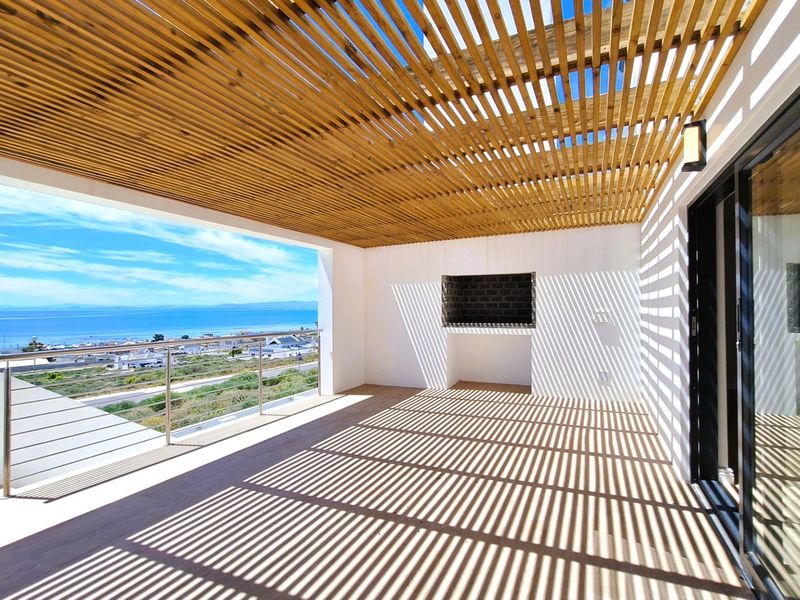 Spacious covered balcony featuring a timber slat pergola, built-in braai, and stainless steel balustrade, offering expansive coastal views.