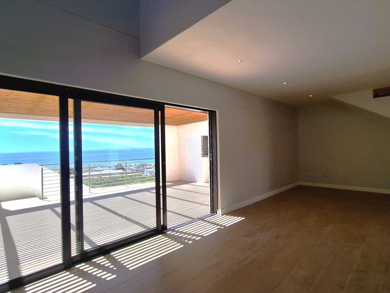 Spacious open-plan living area featuring modern hardwood flooring, recessed lighting, and large sliding glass doors opening onto a scenic balcony with ocean views.