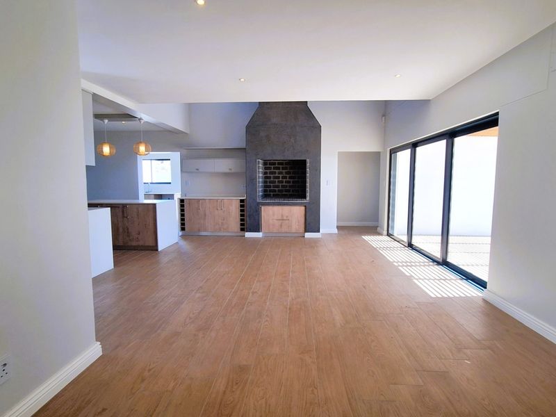 Spacious open-plan living area featuring wood-look tile flooring, a modern built-in fireplace, and large sliding glass doors leading to the outdoor space.