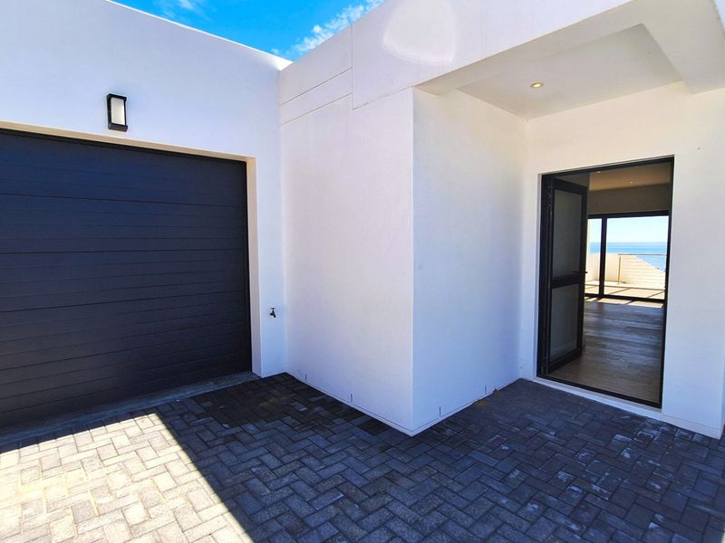 Modern front entrance featuring a dark sectional garage door, paved driveway, and a glass door providing a view through to the ocean.