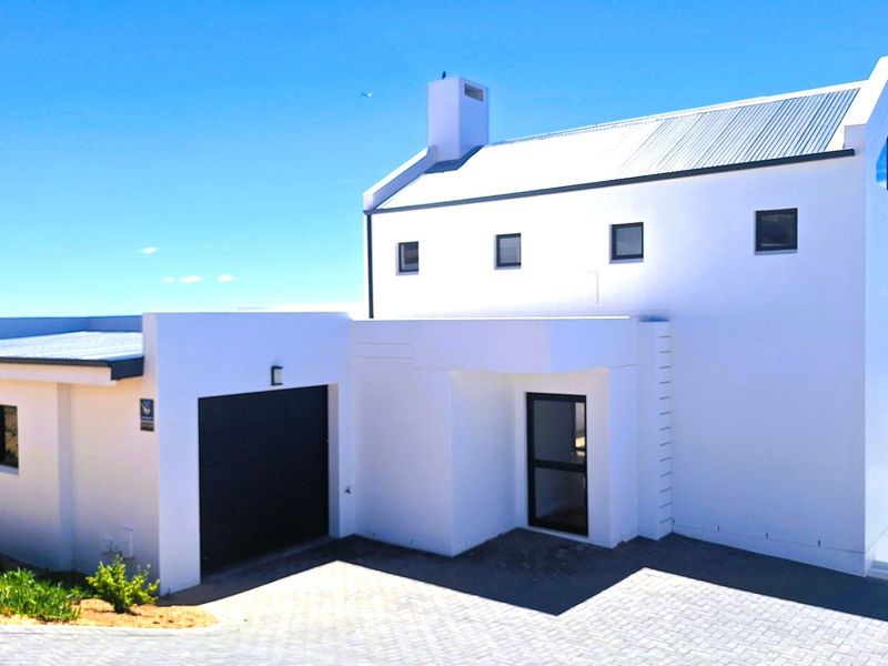 Modern white house exterior featuring a clean architectural design, corrugated metal roof, integrated garage, and paved driveway with coastal views.