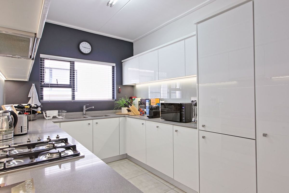 Modern kitchen featuring high-gloss white cabinetry, stone countertops, a gas hob, and integrated lighting, offering a clean and functional culinary space.