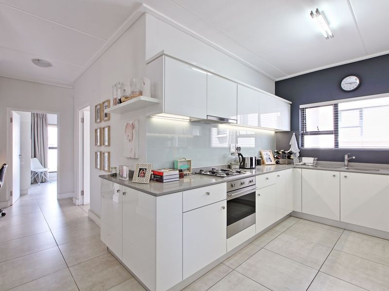 Modern kitchen featuring glossy white cabinetry, stone countertops, glass splashback, built-in oven, gas hob, and tiled flooring.
