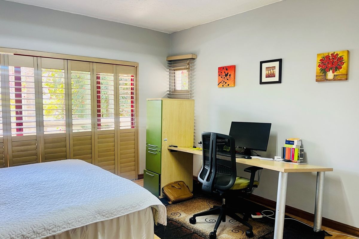 A functional bedroom featuring light-toned walls, wooden plantation shutters, and a built-in desk area, suitable for use as a home office or guest room.