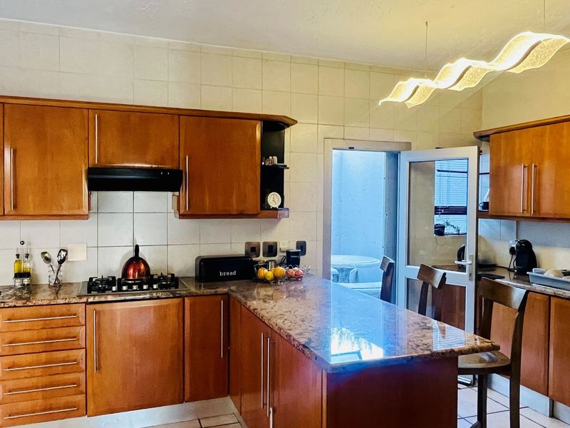 A functional kitchen featuring wooden cabinetry, granite countertops, a gas hob with extractor fan, and direct access to an outdoor area.