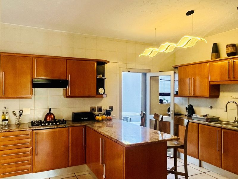 A functional kitchen featuring wooden cabinetry, granite countertops, a gas hob, and an integrated extractor fan, with direct access to an outdoor area.