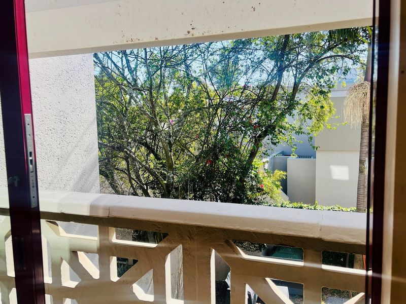 A view from an interior space looking out onto a balcony with a decorative concrete balustrade and surrounding garden greenery.