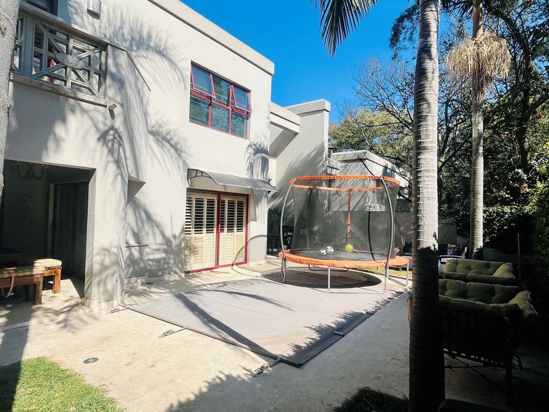 Rear exterior view of the house featuring a paved patio area, covered terrace, and established garden surroundings.