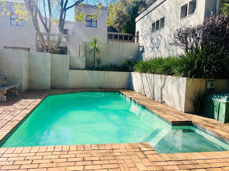 A private swimming pool area featuring brick paving, a built-in step section, and surrounding retaining walls with established garden beds.