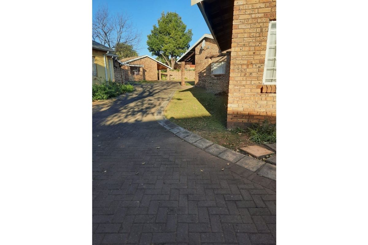 A view of the townhouse complex exterior featuring face brick construction, a paved driveway, and established lawn areas.