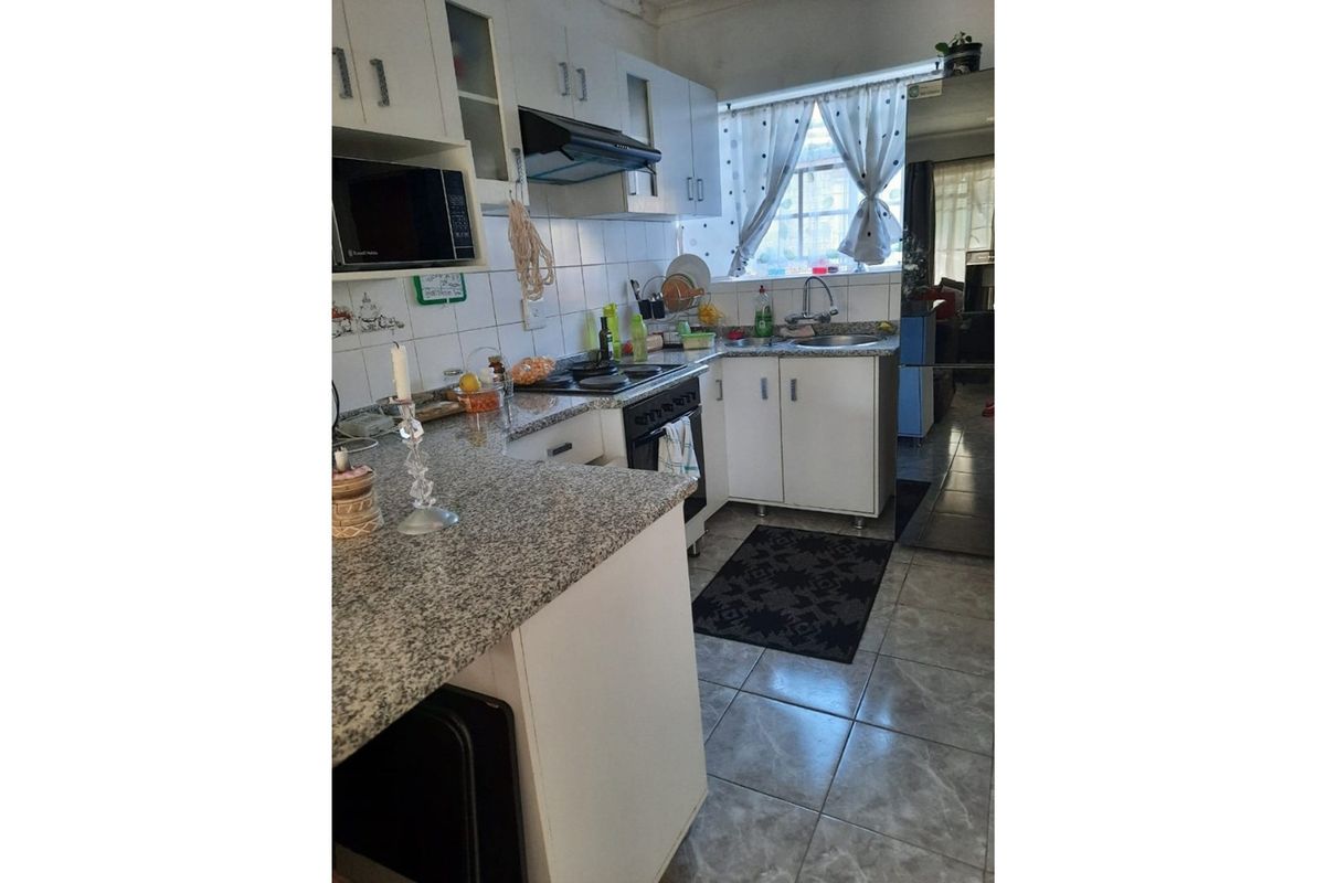 Functional kitchen featuring granite countertops, built-in cabinetry, a stainless steel sink, and integrated cooking appliances with tiled finishes throughout.