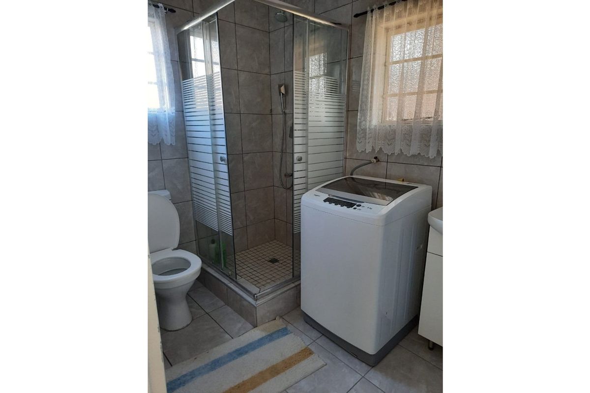 A functional bathroom featuring a glass shower enclosure, toilet, and basin with tiled finishes throughout.