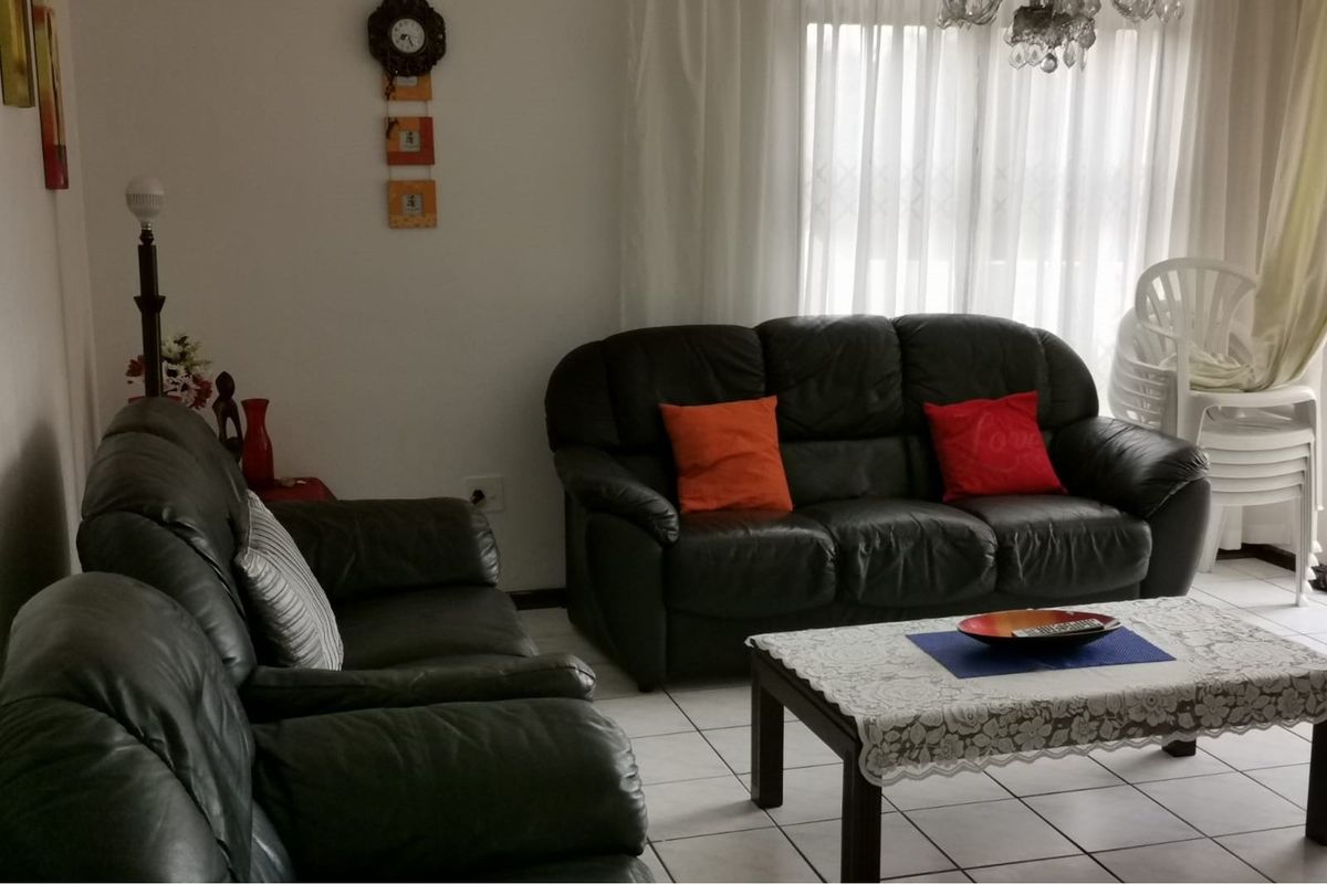 A living room area featuring tiled flooring and large windows with curtains, providing a functional and comfortable space.