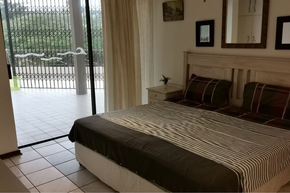 A bedroom featuring tiled flooring and large sliding glass doors that open onto a private balcony with security gate.