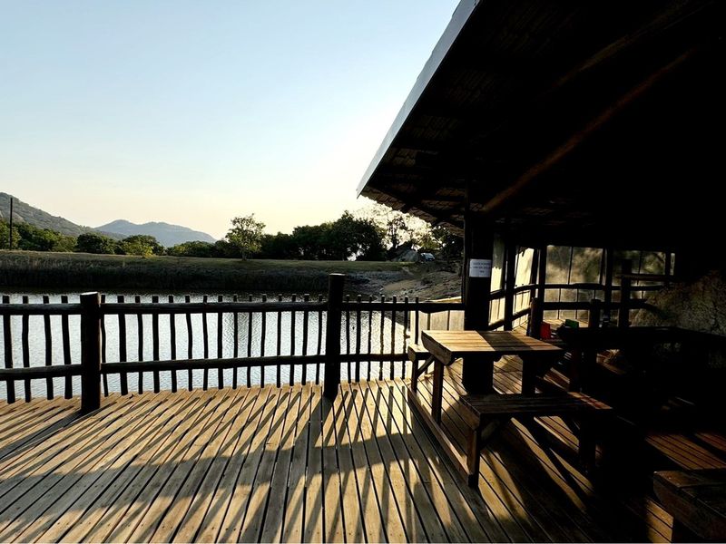 A covered wooden deck overlooking a tranquil dam, featuring rustic timber railings and a peaceful rural landscape view.