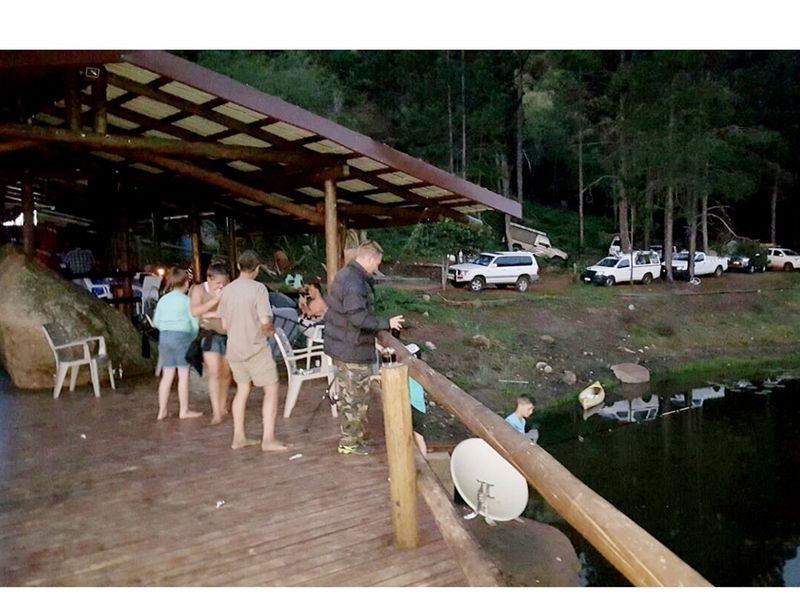 A rustic wooden deck patio overlooking a tranquil dam, featuring a covered timber structure and natural rock integration.