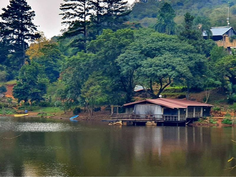A scenic view of a rustic cabin situated on the edge of a tranquil lake, surrounded by lush forest and natural landscape.
