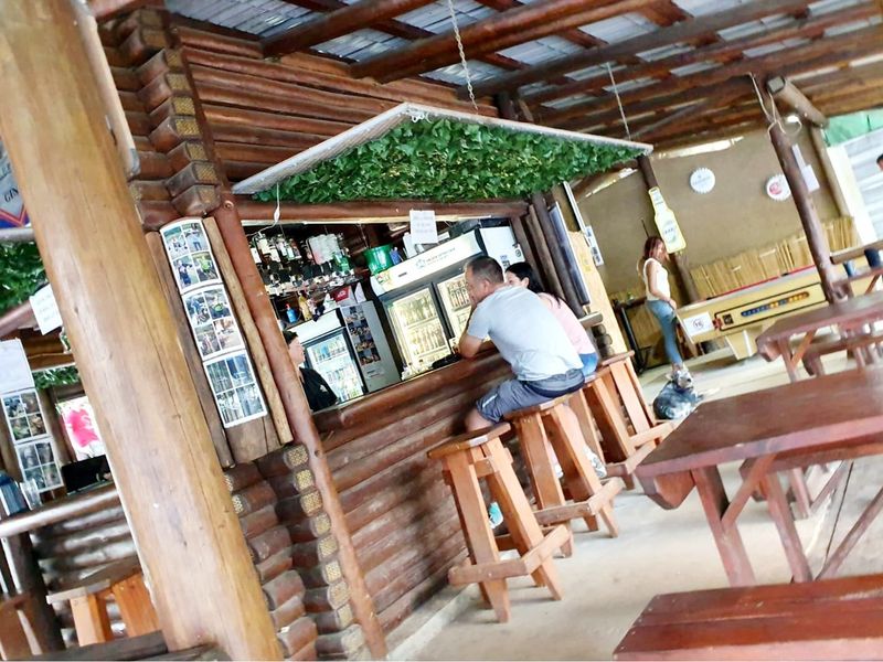 A rustic, open-air bar area featuring log-style construction, a built-in service counter, and a covered timber roof structure.