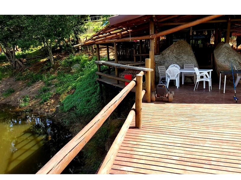A rustic timber deck overlooking a natural pond, featuring integrated wooden railings and a covered outdoor area built into the landscape.