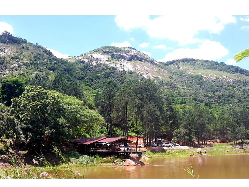 Scenic view of a rustic structure situated on the edge of a tranquil lake, surrounded by lush forest and mountainous terrain.