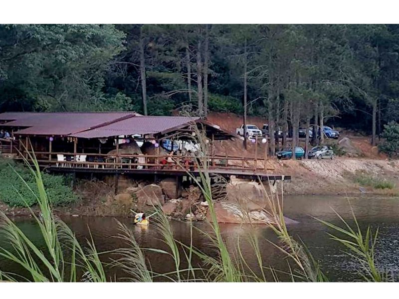 A rustic waterfront structure featuring a large covered deck overlooking the lake, set within a natural wooded landscape.