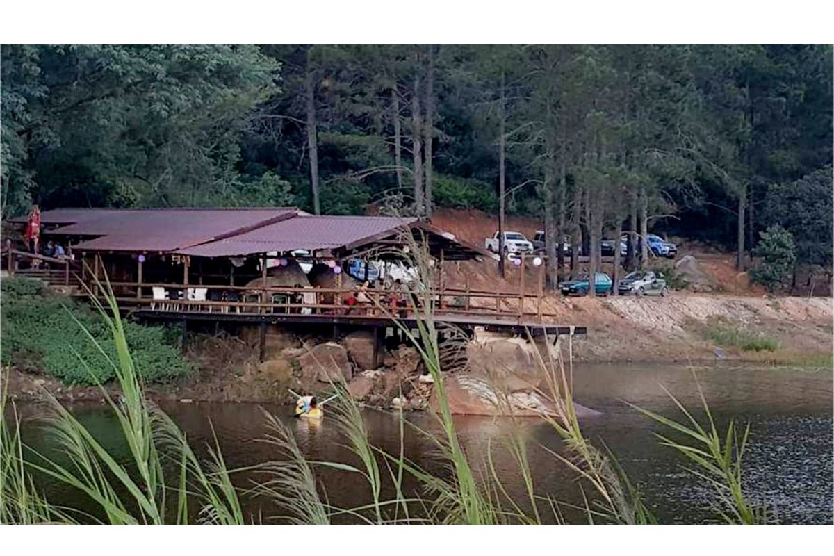 A rustic waterfront structure featuring a large covered deck overlooking the lake, set within a natural wooded landscape.