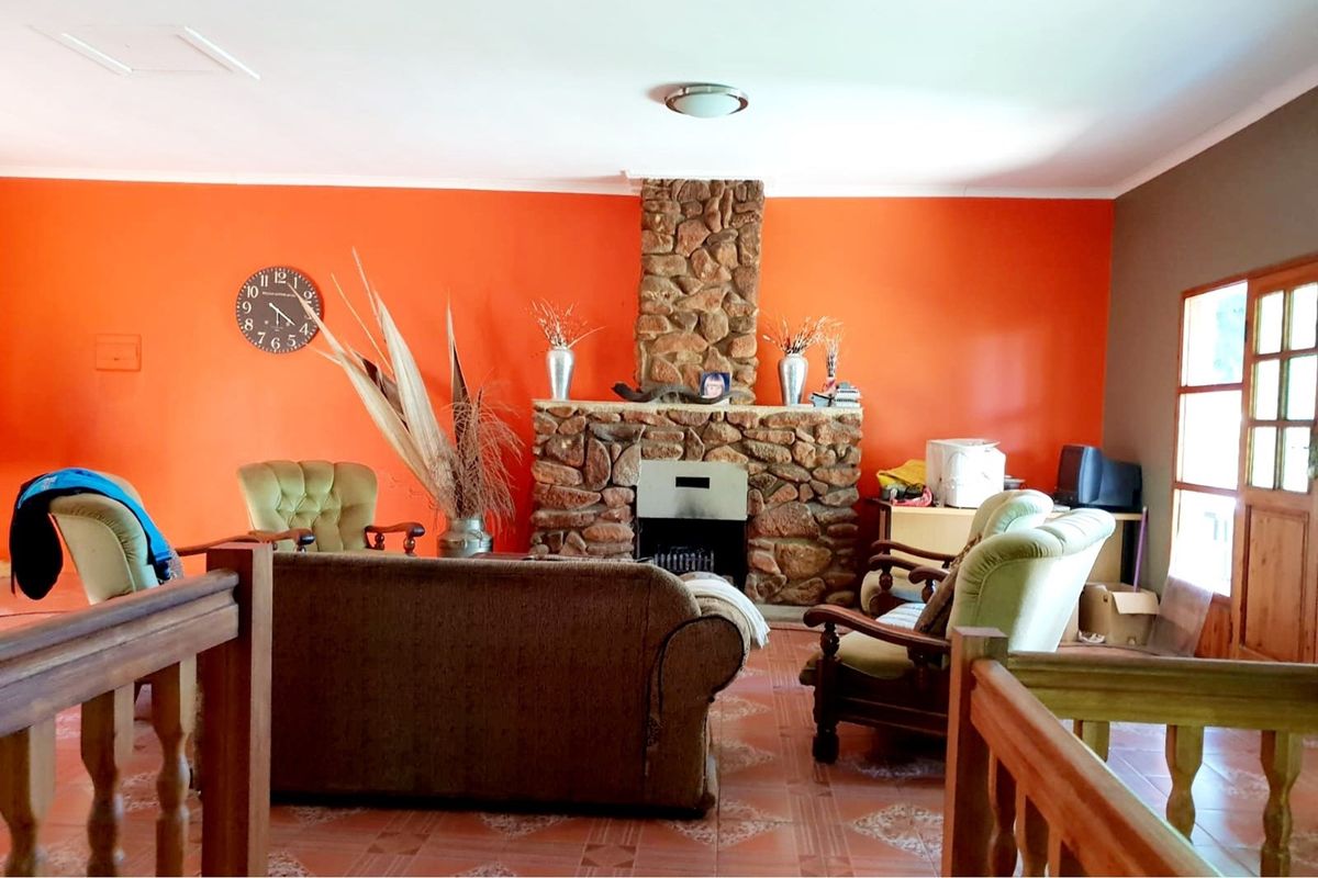 A living room featuring a prominent stone-clad fireplace, tiled flooring, and a wooden staircase railing.