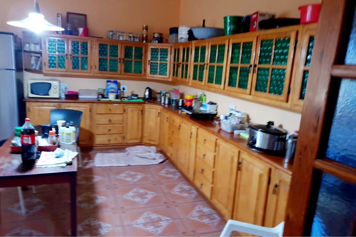 A functional kitchen featuring extensive wooden cabinetry with green glass inserts, tiled flooring, and ample counter space for food preparation.