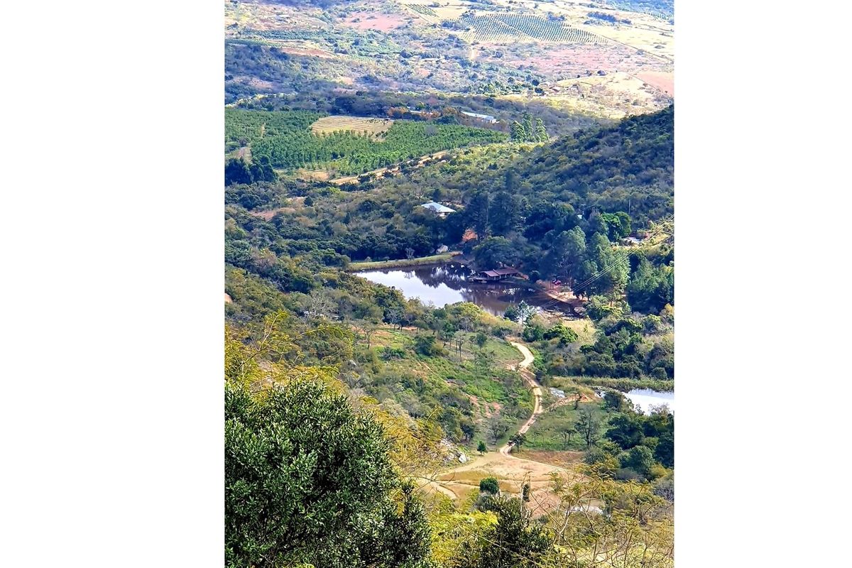 An elevated aerial view showcasing the expansive farm landscape, featuring natural vegetation, rolling hills, and a serene dam.
