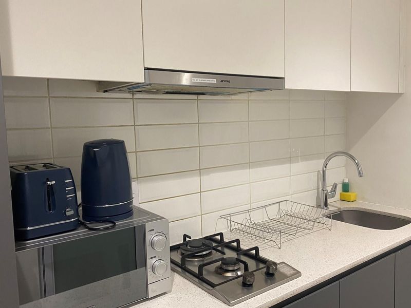 A compact kitchen featuring white cabinetry, a gas cooktop, stainless steel extractor fan, stone-look countertop, and a modern sink with a chrome faucet.