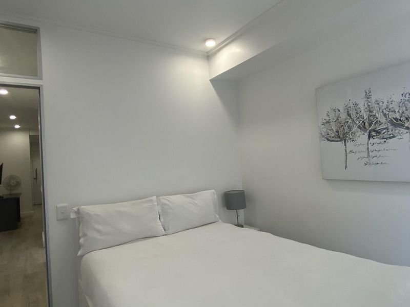 A clean and neutral bedroom featuring recessed ceiling lighting and a doorway leading to an adjacent hallway.
