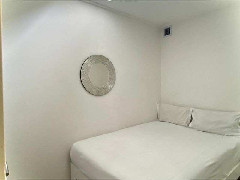 A compact bedroom featuring plain white walls and a built-in ventilation vent.