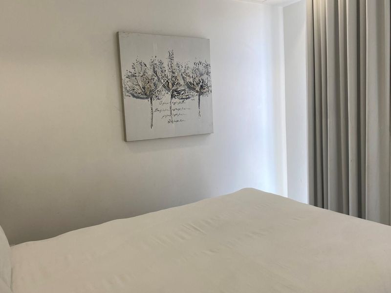 A bright and neutral bedroom featuring floor-to-ceiling curtains and clean finishes, offering a comfortable and minimalist living space.