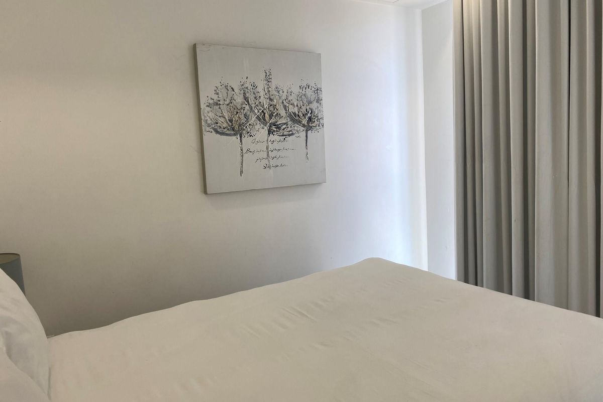 A bright and neutral bedroom featuring floor-to-ceiling curtains and clean finishes, offering a comfortable and minimalist living space.