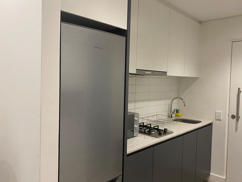 Compact modern kitchen featuring sleek two-tone cabinetry, stone countertops, a built-in gas cooktop, and an integrated extractor fan.