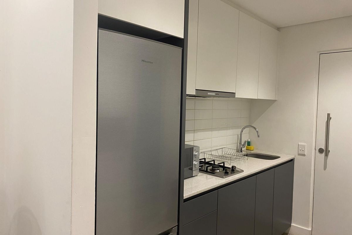 Compact modern kitchen featuring sleek two-tone cabinetry, stone countertops, a built-in gas cooktop, and an integrated extractor fan.