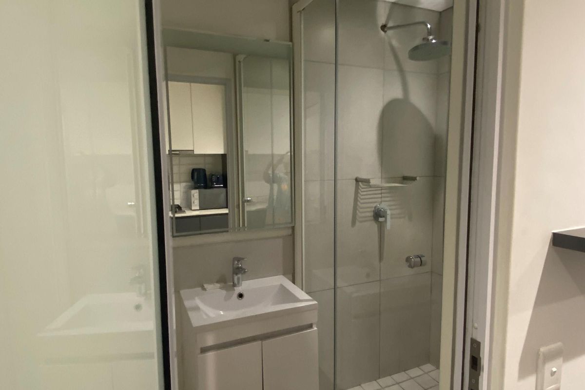 A compact modern bathroom featuring a glass-enclosed shower, a wall-mounted vanity with a basin, and a mirrored cabinet.