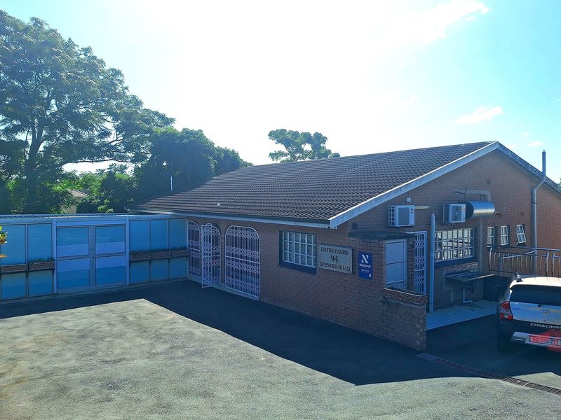 Exterior view of the townhouse complex featuring brick facade, tiled roof, security gates, and paved driveway area.
