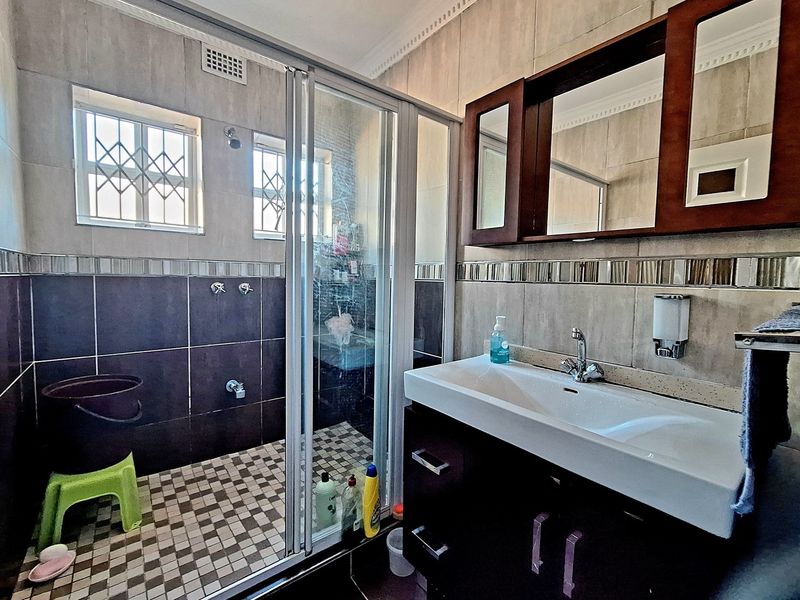 A functional bathroom featuring a glass-enclosed shower, a modern vanity with integrated basin, and tiled walls with decorative mosaic accents.