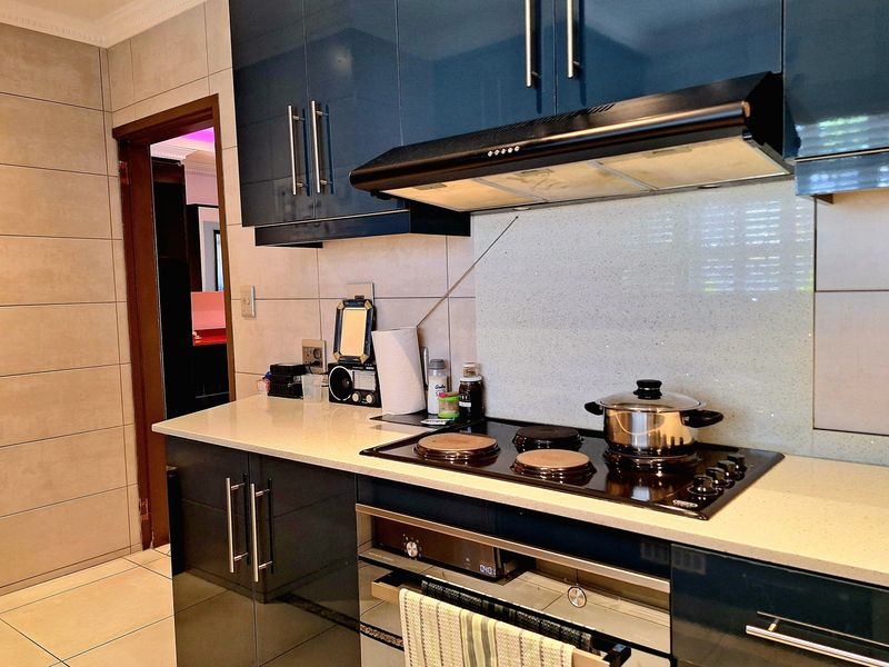 Modern kitchen featuring high-gloss blue cabinetry, stone countertops, a built-in electric hob, and an integrated extractor fan.