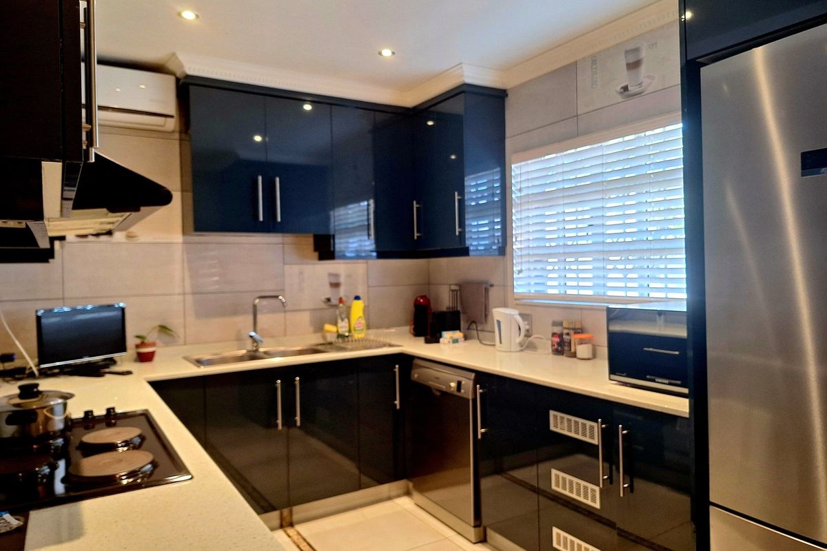 Modern kitchen featuring dark high-gloss cabinetry, stone countertops, integrated stainless steel appliances, and recessed ceiling lighting.