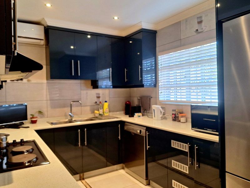 Modern kitchen featuring dark high-gloss cabinetry, stone countertops, integrated stainless steel appliances, and recessed ceiling lighting.