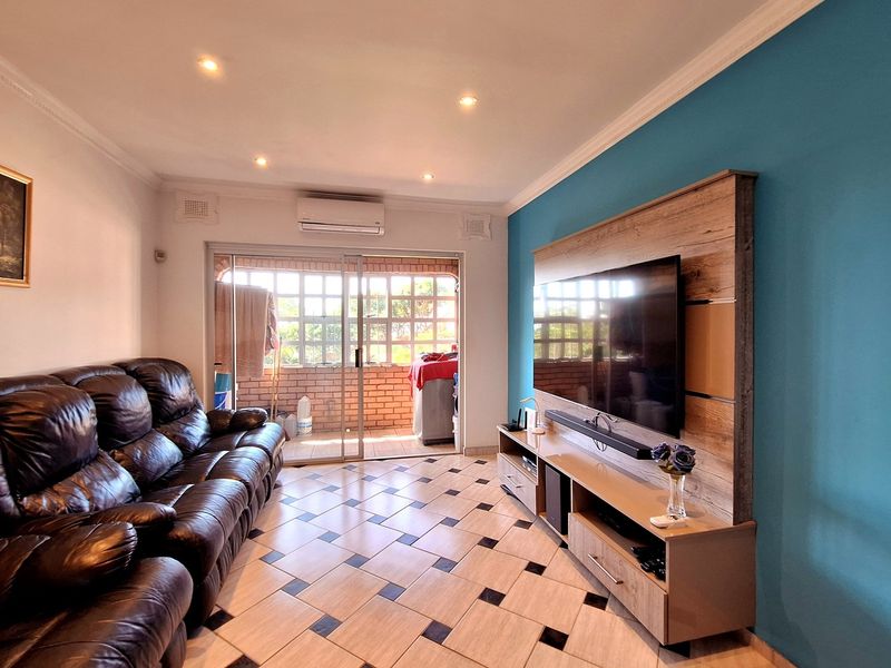 A comfortable living room featuring tiled flooring, recessed downlighting, and a wall-mounted air conditioning unit, with sliding glass doors leading to an outdoor patio area.