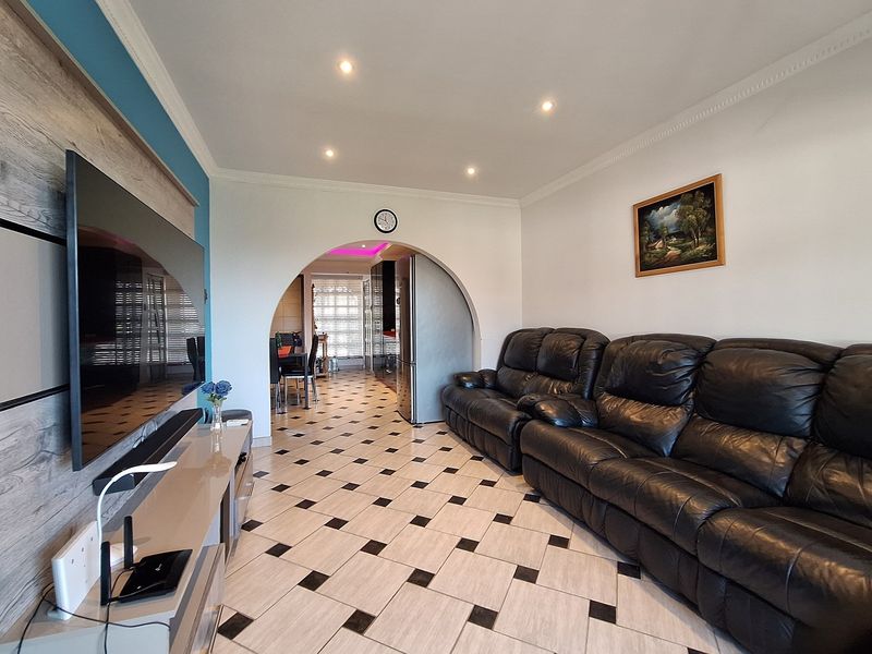 A living room featuring tiled flooring, recessed ceiling lighting, and a decorative arched entryway leading to the adjacent dining area.